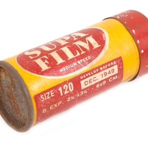 May include: A yellow and red film canister with the text "SUPA FILM" in red lettering. The canister is labeled "Size 120", "Medium Speed", "Develop Before DEC. 1949", "8 Exp. 2 1/2 x 3 1/4 - 6x9 CM."