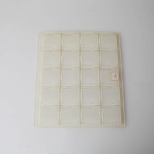 May include: A rectangular, semi-translucent white plastic storage tray featuring a grid of twenty individual square compartments arranged in four rows and five columns, with a small rectangular label affixed to one of the interior sections.