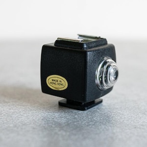 May include: A black flash unit with a silver lens and a gold sticker that reads "Made in Hong Kong".