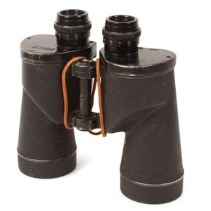 Puede incluir: Binoculares negros con una correa de cuero marrón. Los binoculares tienen un acabado texturizado y un anillo de ajuste de enfoque en cada lente.