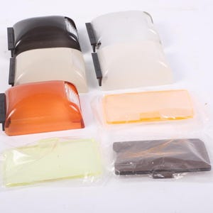 May include: A collection of automotive light covers in various colors, including brown, beige, orange, and yellow. The covers are rectangular and have a curved design. Some are packaged in clear plastic.