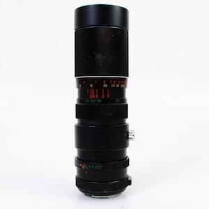 May include: A black camera lens with a silver ring and red markings. The lens has a depth of field scale and a focus ring.