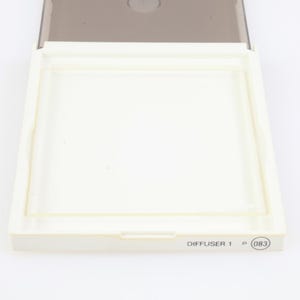 May include: A white plastic diffuser case with a clear plastic insert and a grey lid. The text "DIFFUSER 1" and the number "083" are printed on the bottom right corner of the case. The case is open.