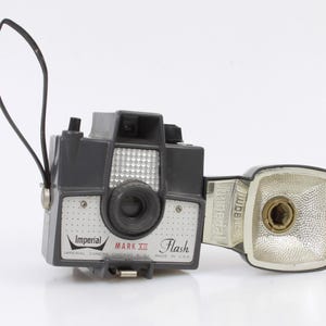 May include: A black and silver Imperial Mark III Flash camera with a built-in flash unit. The camera has a black strap and a silver lens.