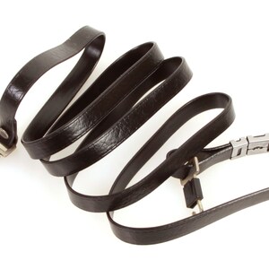 May include: A black leather camera strap with silver metal clasps. The strap is coiled and ready to be attached to a camera.