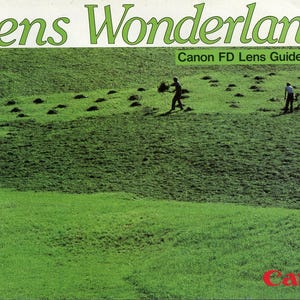 Könnte beinhalten: Ein Softcover-Buch mit dem Titel Lens Wonderland Canon FD Lens Guide Book. Das Cover zeigt ein grünes Feld mit mehreren arbeitenden Personen, ein kleines schwarzes Quadrat mit dem Buchstaben E und das rote Canon-Logo unten rechts.