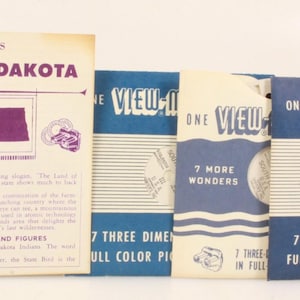 May include: A collection of vintage View-Master reels and a booklet. The booklet, titled "South Dakota," features purple text and a map of the state. The reels are blue and white, with text that reads "7 Three Dimension Full Color Pictures."