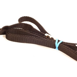 May include: A black camera strap with a metal buckle and a blue rubber band.