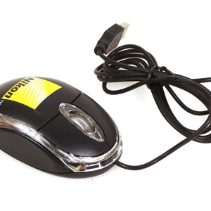 Puede incluir: Ratón de ordenador Nikon negro con un borde de plástico transparente y un logotipo amarillo y blanco. El ratón tiene una rueda de desplazamiento y un cable negro con un conector USB.