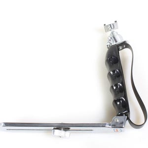 May include: A black and silver camera grip with a rubber handle and a strap. The grip has a cold shoe mount on top and a quick release plate on the bottom.