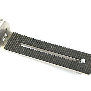 May include: A silver metal camera tripod plate with a black rubberized grip surface. The plate has a screw hole and a slot for attaching to a tripod.