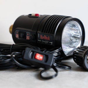 May include: A black Britek H-48F flash unit with a white reflector, a black power cord, and a black on/off switch.
