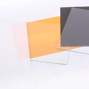 Könnte beinhalten: Eine Ansammlung von quadratischen und rechteckigen, durchscheinenden und undurchsichtigen Blättern in verschiedenen Farben, darunter Weiß, Orange, Grau und Schwarz. Die Blätter sind leicht überlappend angeordnet und zeigen ihre unterschiedlichen Texturen und Opazitäten.