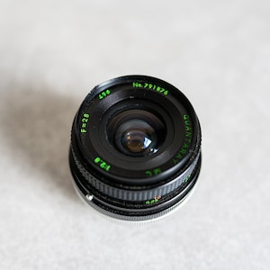 May include: A black camera lens with green text that reads "QUANTARAY MC 1:2.8 12.5mm F=28 No. 791876".