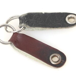 May include: Two leather keychains with metal rings. One keychain is brown and the other is black.