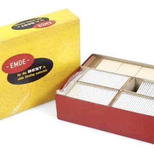 May include: A vintage set of slide binding materials in a yellow box with the text "EMDE" and "for the BEST is slide binding materials." The set includes a red box with dividers holding numerous slides and other components.