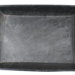 May include: A rectangular, black tray with slightly curved edges. The tray has a matte finish and appears to be made of metal. The corners are squared, and the overall design is simple and functional.