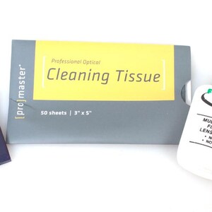 May include: A set of optical cleaning supplies, including a brush with a blue handle, a package of cleaning tissues, and a bottle of lens cleaner. The cleaning tissue package is labeled "Cleaning Tissue" and measures 3" x 5". The lens cleaner bottle is white with a green cap.