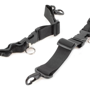 May include: Two black nylon straps with plastic buckles and metal key rings. One strap has a hook clasp. The straps are designed to be adjustable and are likely used for securing items or as a carrying strap.