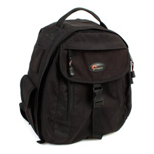 Peut inclure: Sac à dos noir pour appareil photo avec une grande poche avant et une petite poche sur le côté. Le sac à dos a une sangle noire avec une boucle et le mot "Lowepro" est imprimé sur la poche avant.