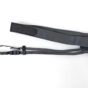 Puede incluir: Una correa de cámara negra con cierre de velcro y longitud ajustable. La correa tiene una hebilla de plástico negra.