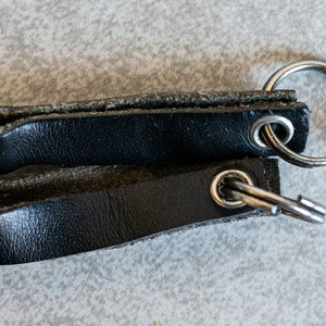 以下が含まれることがあります： 銀色の金属リングと銀色のキーリングが付いた黒い革のキーホルダー2個