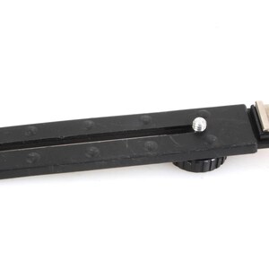 Puede incluir: Accesorio de cámara negro con zapata metálica y riel deslizante. Cuenta con un tornillo de ajuste y una base texturizada. Mide aproximadamente 15 cm de largo, diseñado para montar equipos.