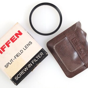 May include: A Tiffen split-field lens kit, including a black screw-in filter, a brown leather case, and the original box. The box is white with red and black text. The filter is a circular shape.