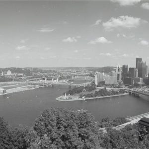 Op de afbeelding: Zwart-wit panoramische foto van een stadsgezicht met bruggen, rivieren en gebouwen. De afbeelding toont een breed beeld van het stedelijke landschap, met de nadruk op architectuur en natuurlijke elementen.