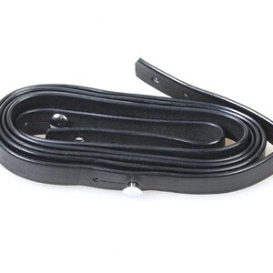 May include: A black leather strap with a silver metal buckle. The strap is rolled up and ready to be used.