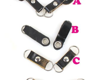 May include: Four different types of leather key fobs with metal rings. The fobs are black and brown leather with metal rivets and eyelets. The fobs are labeled A, B, C, and D.