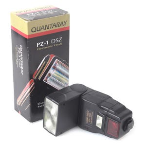 May include: A black Quantaray PZ-1 DSZ electronic flash with a box. The flash has a rectangular head with a clear lens and a red panel. The box is black with yellow and red accents and the text "QUANTARAY PZ-1 DSZ Electronic Flash".