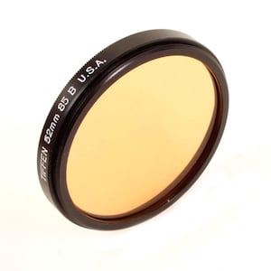 May include: A Tiffen 52mm 85 B U.S.A. camera filter. The filter has a black rim and a light orange-tinted glass. The filter is circular and angled slightly, set against a white background.