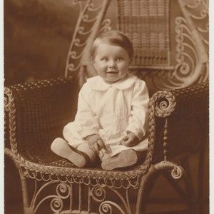 Cute but Scary Baby Smiling on an Ornate Chair. Sepia Toned Print.
