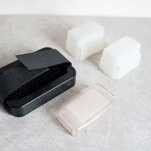 Könnte beinhalten: Ein Set mit vier Blitzdiffusor-Zubehör für die Fotografie. Das Set enthält ein schwarzes Wabengitter, einen weißen Diffusor, eine weiße Rückwand und einen klaren Diffusor.