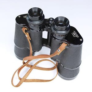 Puede incluir: Binoculares negros con una correa de cuero marrón. Los binoculares tienen el texto "ASAHI PENTAX 7x50" impreso en el lateral.