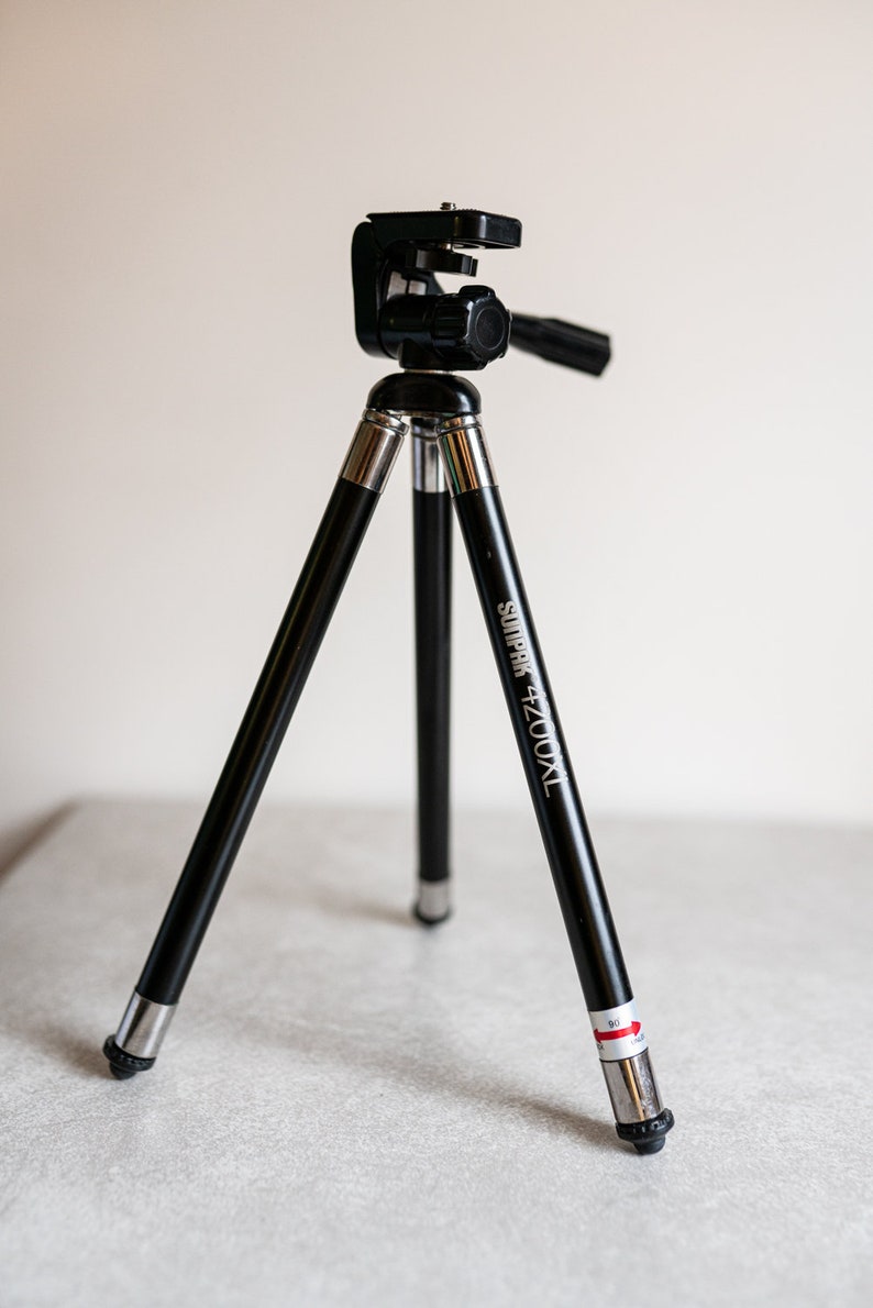 Puede incluir: Un tr&iacute;pode negro con detalles plateados y el texto "Sunpak 4200XL" impreso en una de las patas. El tr&iacute;pode est&aacute; extendido y listo para usar.