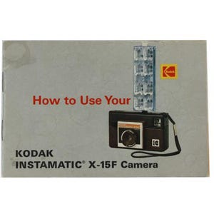 Puede incluir: Una cámara Kodak Instamatic X-15F negra y plateada con flash incorporado. La portada del manual de instrucciones dice "How to Use Your Kodak Instamatic X-15F Camera".
