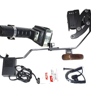 May include: A black and silver camera flash unit with a bracket, wooden handle, and power supply. Includes a black cord, a small white card with red text, and a coiled cable.