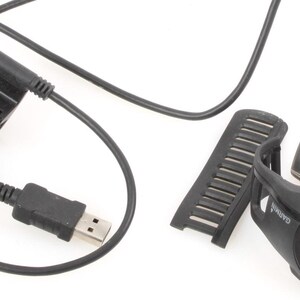 Puede incluir: Un reloj Garmin Forerunner negro con un cable de carga USB y una pulsera negra.