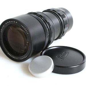 K&ouml;nnte beinhalten: Ein schwarzes Leica Tele-Elmarit 135mm f/3.5 Objektiv mit einer silbernen Objektivkappe und einer schwarzen Objektivkappe mit dem Leica Logo.