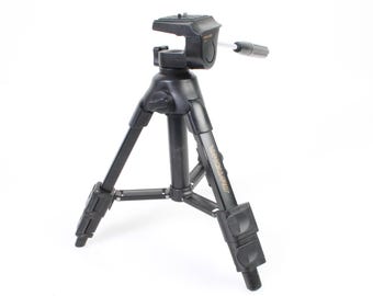 May include: A black tripod with a silver quick release plate and a black handle. The tripod has a gold label that says "Vanguard" on it.