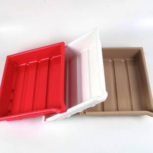 May include: Three rectangular plastic trays arranged in a row, featuring a bright red tray on the left, a white tray in the center, and a tan tray on the right. Each tray has a smooth, glossy finish with vertical ridges along the bottom surface.