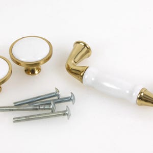 May include: Set of four gold-toned cabinet knobs with white ceramic inserts. Two knobs are round and two are rectangular. The set also includes four screws.