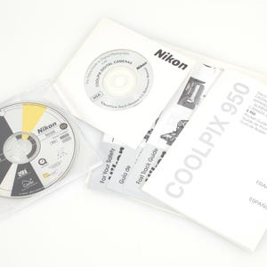 May include: A collection of Nikon camera accessories, including a CD-ROM, manuals, and a quick start guide. The CD-ROM is in a clear plastic sleeve. The manuals are white with black text and a yellow accent. The product is for the Coolpix 950 camera.