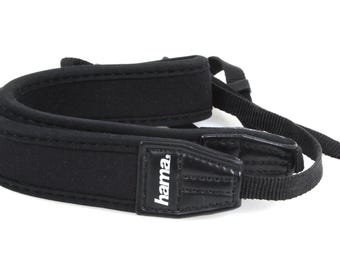 May include: Black camera neck strap with a padded shoulder rest. The strap features the brand name "hama." The strap is made of durable materials and is designed for comfort and security.