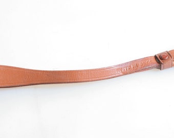 May include: A brown leather camera strap with a metal and brass attachment. The strap has the text "Made in Italy" embossed on it.