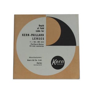 Könnte beinhalten: Eine weiße und braune Schachtel mit einem schwarzen und weißen Kreis in der Mitte. Die Schachtel ist mit "Kern-Paillard Lenses" und "f = 18-86 mm Paillard-Bolex 16 mm cameras" beschriftet. Die Schachtel enthält auch den Text "Depth of field table for" und "Manufacturers: Kern & Co. Ltd. Aarau Switzerland".