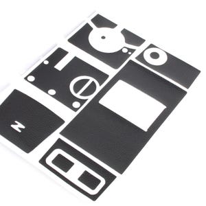 Op de afbeelding: Een set zwarte vinyl auto-interieur trimstukken voor een voertuig. De stukken zijn ontworpen om het dashboard, de deurpanelen en andere gebieden van het interieur te bedekken. De stukken zijn gesneden om te passen bij het specifieke voertuigmodel.
