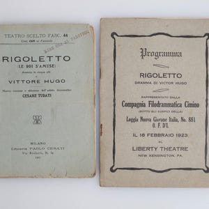 May include: Two vintage Italian opera programs for "Rigoletto" by Victor Hugo. The left program is light blue with text in Italian. The right program is beige with black text and a decorative border. The programs are aged and show signs of wear.